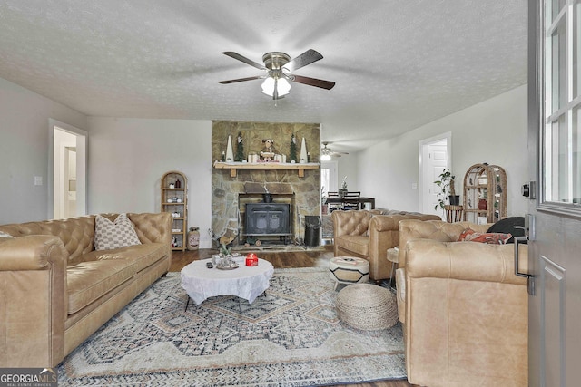 living room with ceiling fan, wood-type flooring, a wood stove, and a textured ceiling