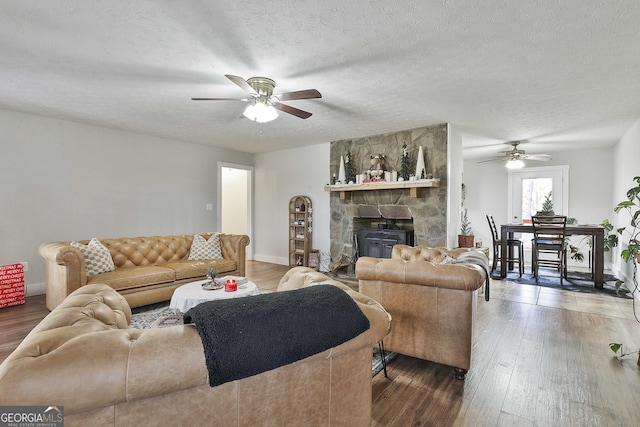 living room with a stone fireplace, ceiling fan, dark hardwood / wood-style flooring, and a textured ceiling