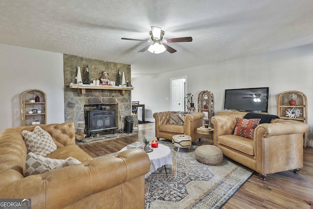 living room featuring hardwood / wood-style floors, a textured ceiling, a wood stove, and ceiling fan