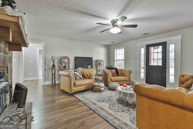 living room featuring a fireplace, a textured ceiling, ceiling fan, and dark wood-type flooring