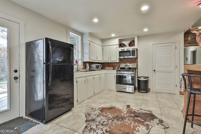 kitchen with sink, light tile patterned floors, tasteful backsplash, white cabinets, and appliances with stainless steel finishes