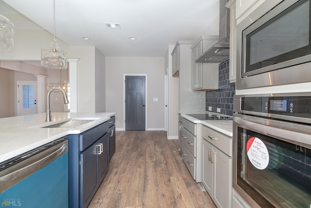 kitchen featuring hardwood / wood-style floors, wall chimney range hood, sink, decorative light fixtures, and stainless steel appliances