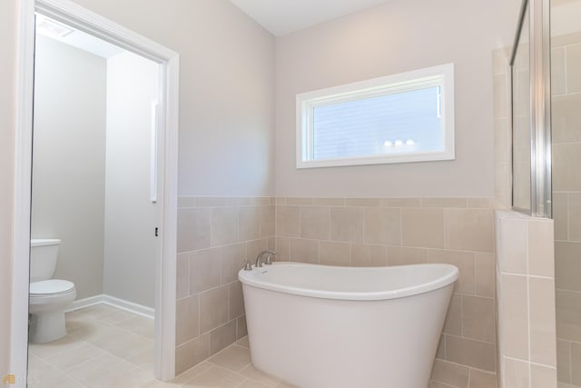 bathroom with tile patterned floors, a bathtub, toilet, and tile walls