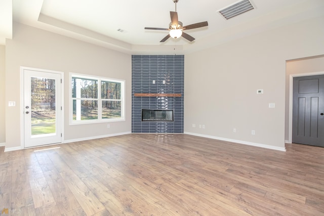 unfurnished living room featuring a tray ceiling, a tile fireplace, ceiling fan, and light hardwood / wood-style flooring