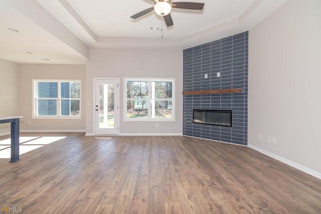 unfurnished living room featuring a tray ceiling, ceiling fan, a fireplace, and wood-type flooring