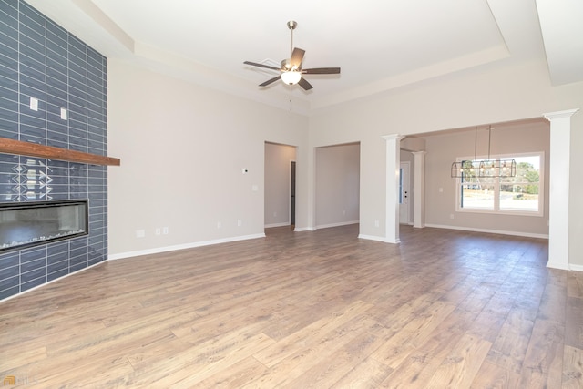 unfurnished living room featuring a fireplace, hardwood / wood-style floors, ceiling fan with notable chandelier, and a tray ceiling