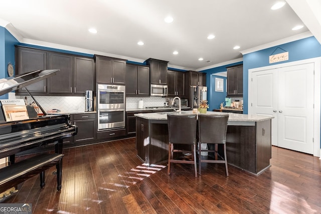 kitchen featuring appliances with stainless steel finishes, dark hardwood / wood-style flooring, tasteful backsplash, light stone counters, and a center island with sink