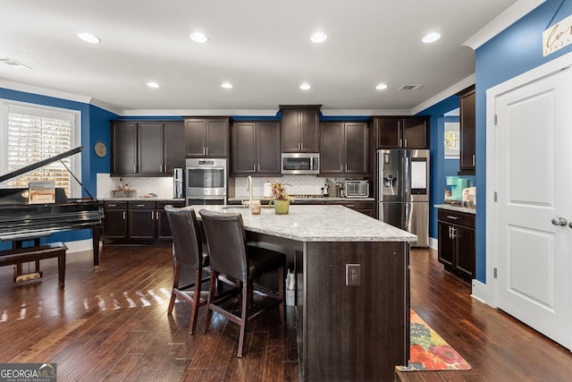 kitchen featuring a center island with sink, dark hardwood / wood-style floors, dark brown cabinetry, and stainless steel appliances