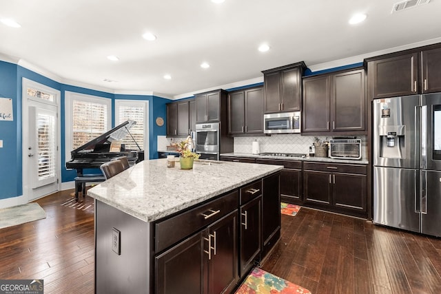 kitchen with backsplash, dark brown cabinets, stainless steel appliances, dark wood-type flooring, and a kitchen island