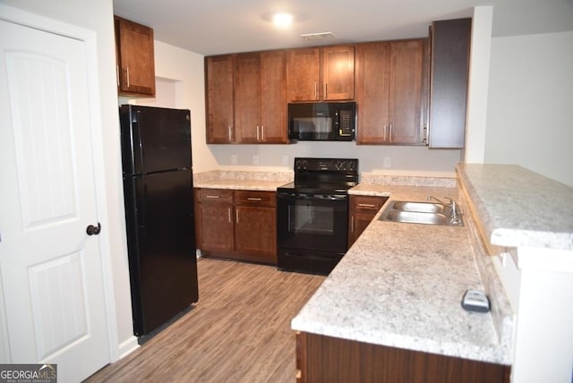 kitchen with kitchen peninsula, sink, light hardwood / wood-style flooring, and black appliances