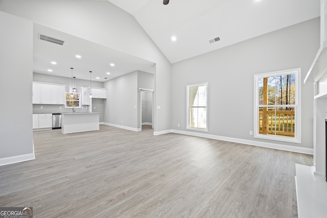 unfurnished living room with a wealth of natural light, high vaulted ceiling, and light wood-type flooring