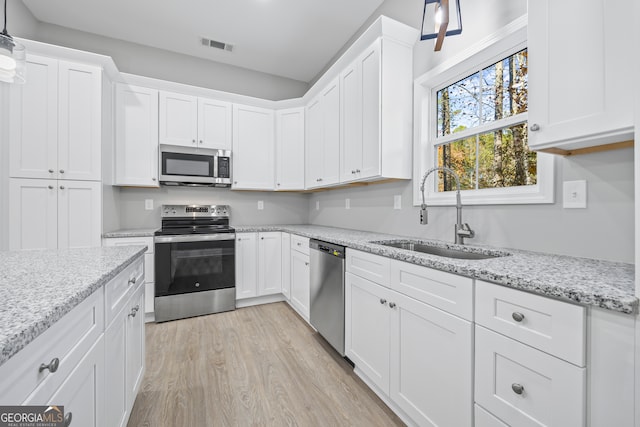 kitchen featuring sink, decorative light fixtures, appliances with stainless steel finishes, light hardwood / wood-style floors, and white cabinets