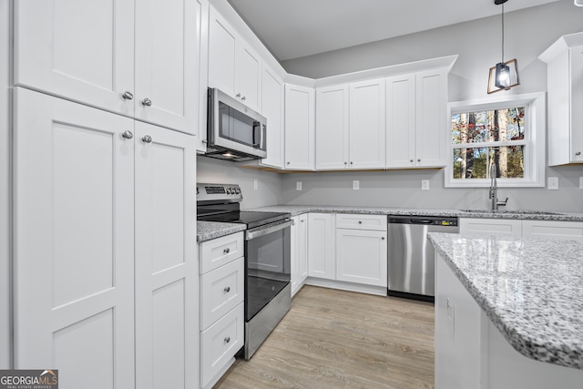 kitchen featuring light hardwood / wood-style flooring, white cabinetry, stainless steel appliances, light stone countertops, and decorative light fixtures