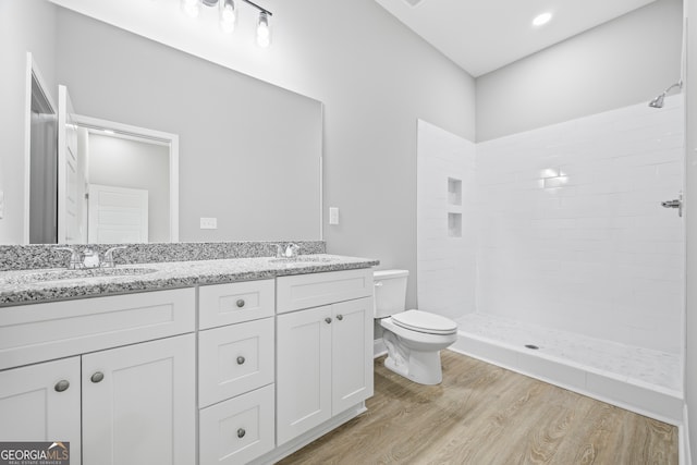 bathroom with tiled shower, vanity, toilet, and wood-type flooring