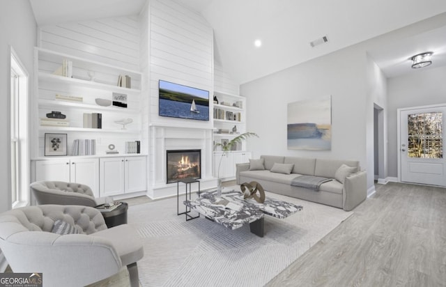 living room with plenty of natural light, built in features, high vaulted ceiling, and light hardwood / wood-style flooring