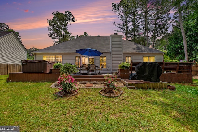 back house at dusk featuring a yard, a hot tub, and a wooden deck