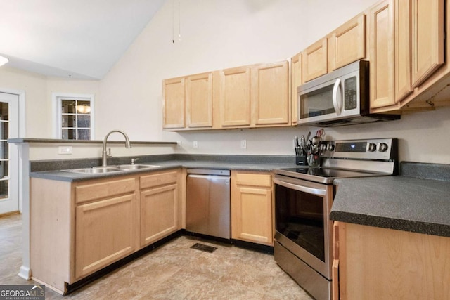 kitchen featuring appliances with stainless steel finishes, vaulted ceiling, light brown cabinetry, and sink