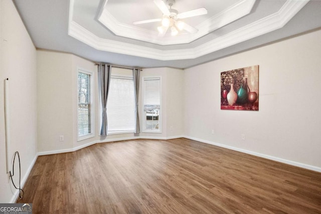 empty room featuring ceiling fan, a raised ceiling, wood-type flooring, and ornamental molding