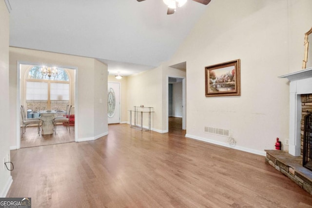 living room with ceiling fan with notable chandelier, a stone fireplace, light wood-type flooring, and high vaulted ceiling