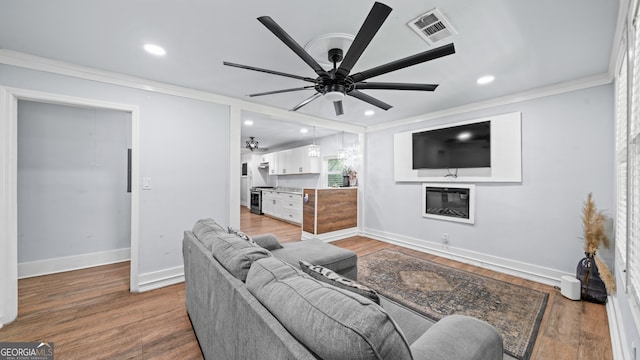 living room with hardwood / wood-style flooring, ceiling fan, and crown molding