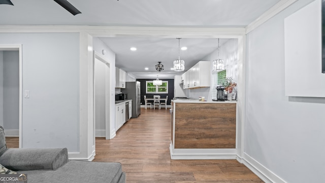 kitchen featuring stainless steel refrigerator, white cabinetry, hanging light fixtures, dark hardwood / wood-style flooring, and crown molding