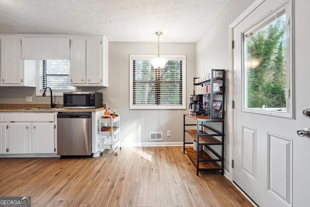 kitchen featuring white cabinets, appliances with stainless steel finishes, decorative light fixtures, and light hardwood / wood-style flooring