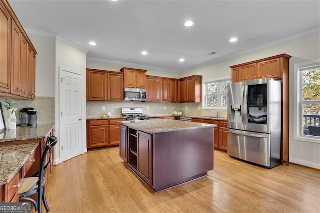 kitchen with appliances with stainless steel finishes, light wood-type flooring, a kitchen island, and plenty of natural light