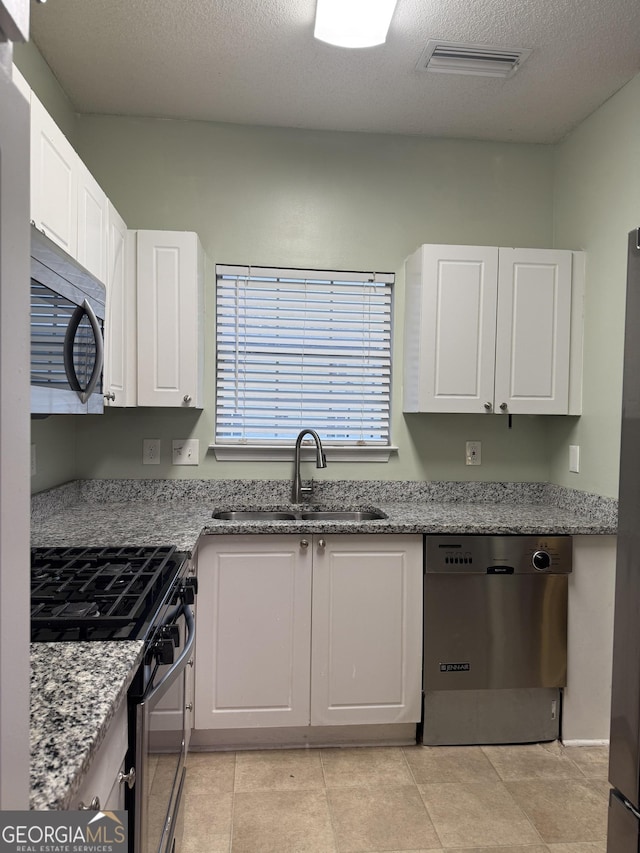 kitchen featuring light stone countertops, a textured ceiling, stainless steel appliances, sink, and white cabinetry