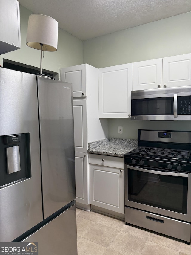 kitchen with light tile patterned floors, a textured ceiling, appliances with stainless steel finishes, light stone counters, and white cabinetry