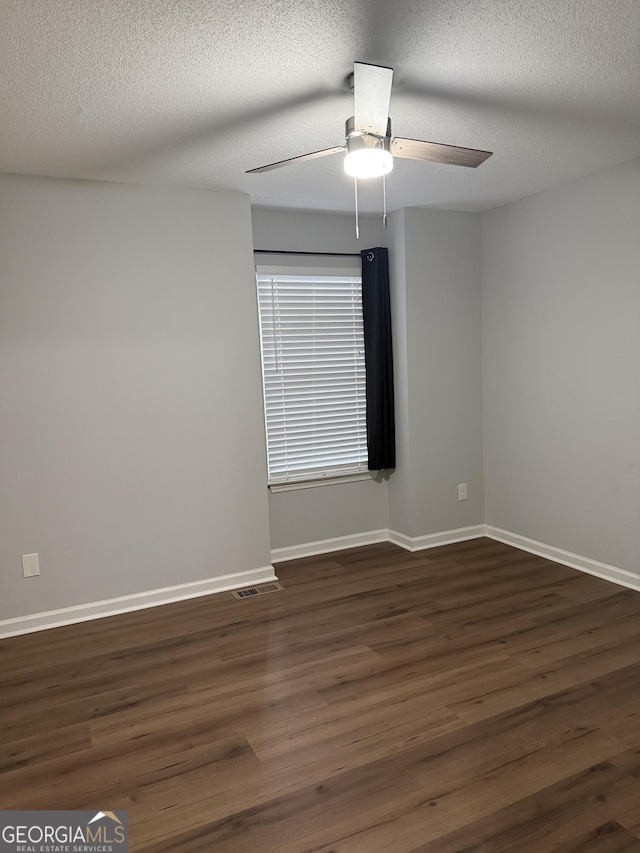 empty room with ceiling fan, dark wood-type flooring, and a textured ceiling