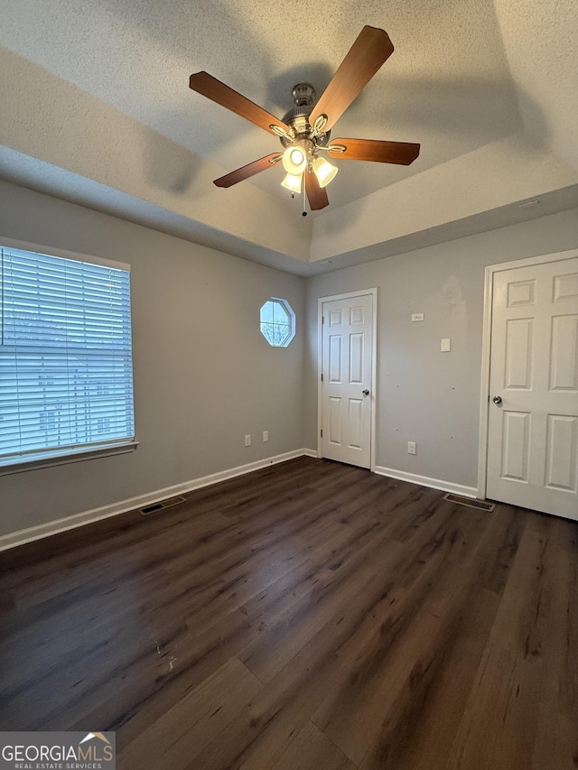 unfurnished bedroom with a textured ceiling, multiple windows, and dark hardwood / wood-style floors