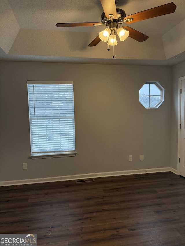 empty room with lofted ceiling, dark wood-type flooring, ceiling fan, a textured ceiling, and a tray ceiling