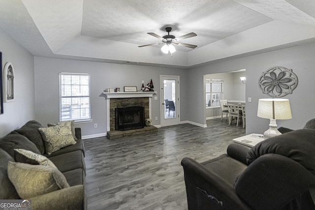 living room featuring a fireplace, dark hardwood / wood-style flooring, a tray ceiling, and ceiling fan