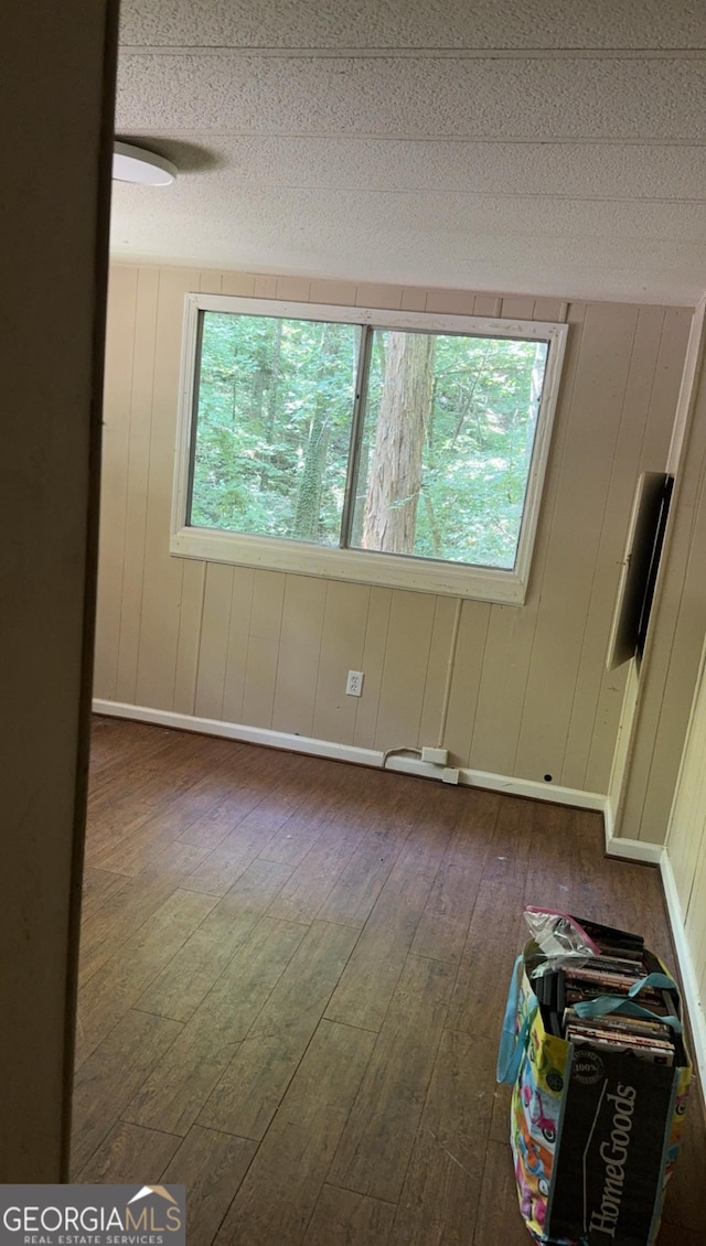 unfurnished room featuring wood walls, dark hardwood / wood-style flooring, and a textured ceiling