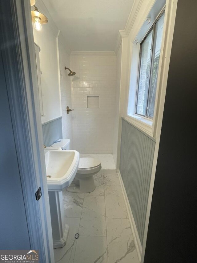 bathroom with toilet, a tile shower, and ornamental molding