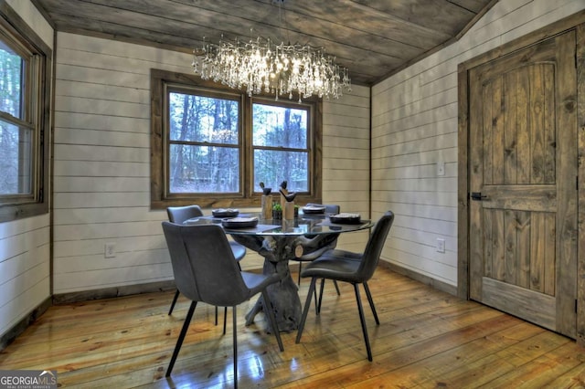 dining space with a chandelier, wooden walls, hardwood / wood-style floors, and a healthy amount of sunlight