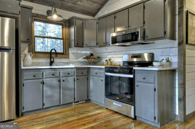 kitchen with gray cabinetry, light wood-type flooring, stainless steel appliances, and vaulted ceiling