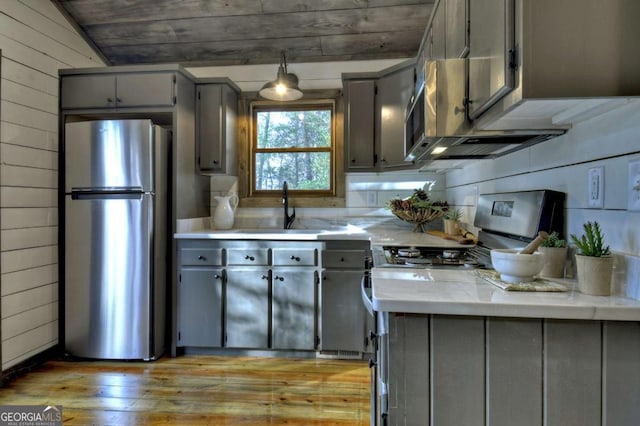 kitchen with sink, stainless steel appliances, gray cabinets, and wood walls