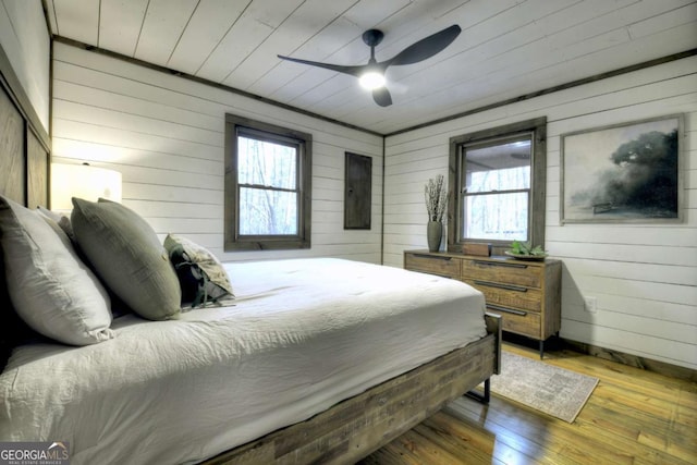 bedroom with hardwood / wood-style flooring, multiple windows, wood walls, and ceiling fan