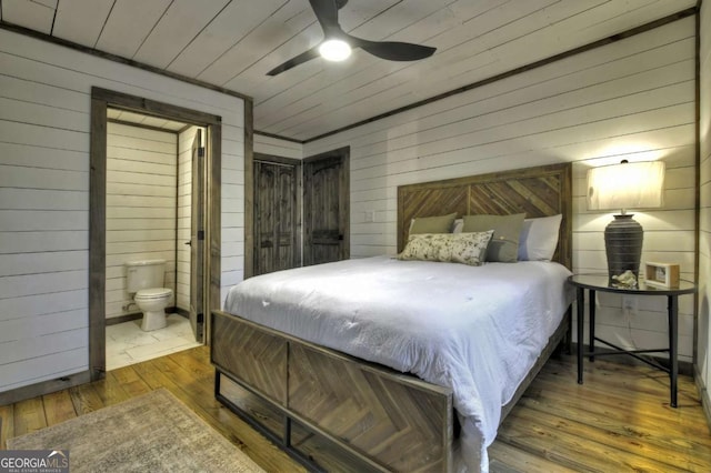 bedroom featuring ensuite bath, ceiling fan, wood walls, and dark hardwood / wood-style floors