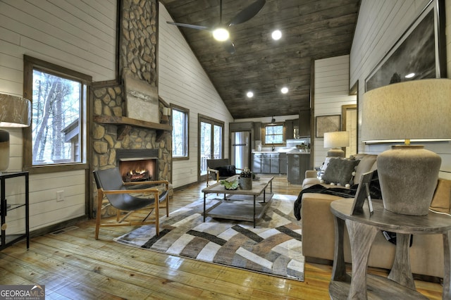 living area featuring wood-type flooring, high vaulted ceiling, a stone fireplace, and wood walls