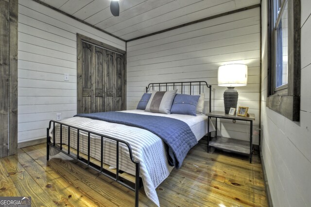 bedroom with ceiling fan, wood walls, and wood-type flooring