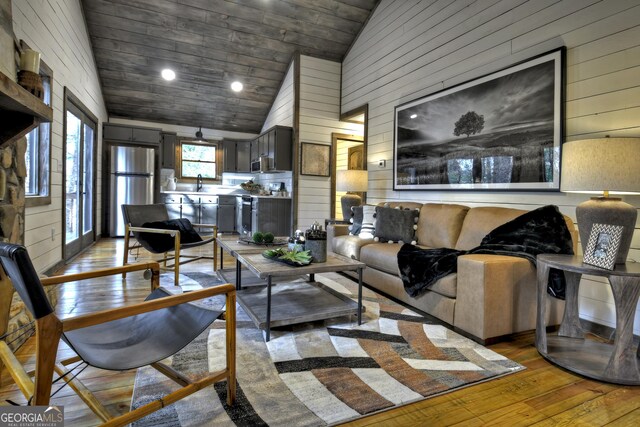 living room featuring wooden ceiling, a stone fireplace, high vaulted ceiling, wood walls, and light hardwood / wood-style floors