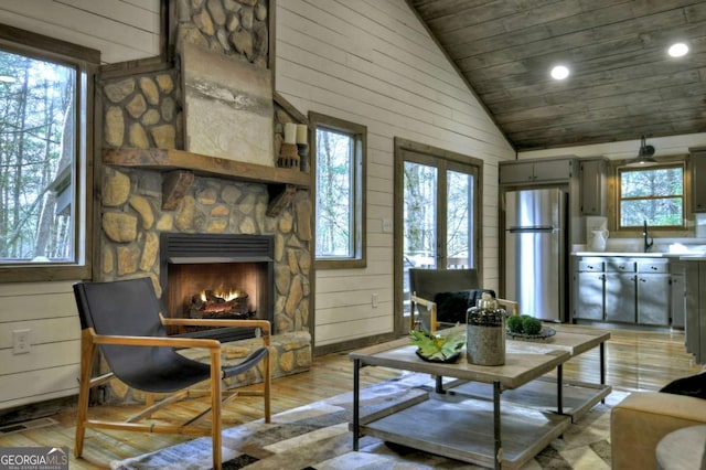 living room featuring a fireplace, high vaulted ceiling, a healthy amount of sunlight, and wood walls