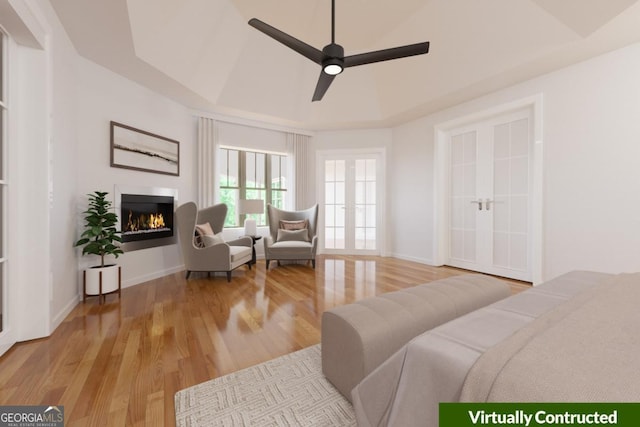 bedroom featuring a tray ceiling, wood finished floors, baseboards, and a lit fireplace