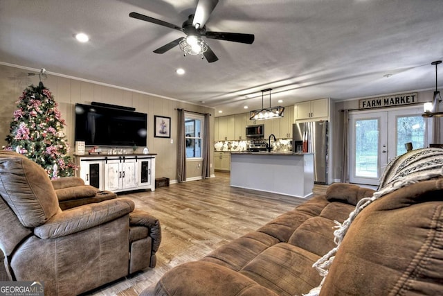 living room featuring ceiling fan, sink, french doors, light wood-type flooring, and ornamental molding