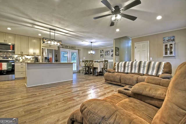 living room with light hardwood / wood-style floors, ceiling fan with notable chandelier, and ornamental molding