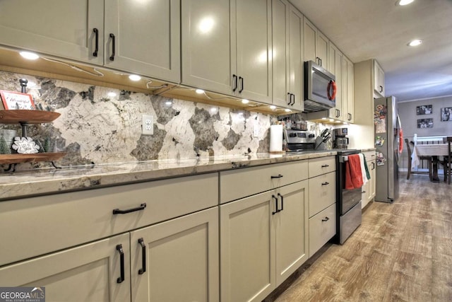 kitchen with tasteful backsplash, light stone countertops, light hardwood / wood-style floors, and appliances with stainless steel finishes