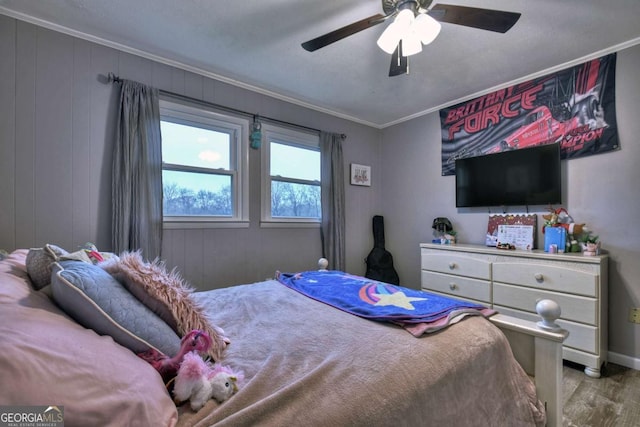 bedroom with light wood-type flooring, ceiling fan, crown molding, and wood walls