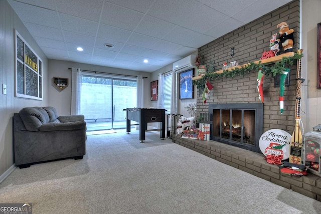 carpeted living room featuring a wall unit AC, a paneled ceiling, and a brick fireplace